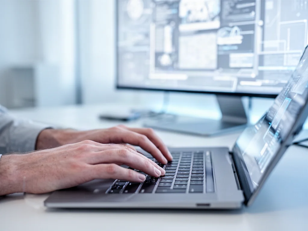 Dłonie piszące na klawiaturze nowoczesnego laptopa w minimalistycznym biurze, ilustrujące pracę z systemem Windows 11.